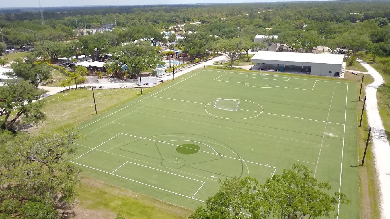 Aerial drone view of Camp Impact's green turf sports field surrounded by trees and camp buildings
